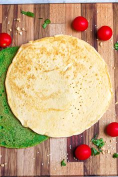 an uncooked tortilla sitting on top of a wooden cutting board next to tomatoes