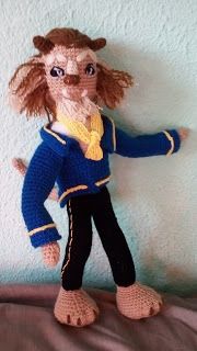 a crocheted doll is dressed in blue and black, standing on a bed