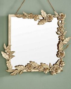 a mirror hanging on the wall with flowers and leaves around it's edge,