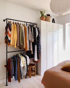 a rack with clothes hanging on it next to a bed in a white walled room