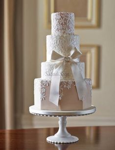 a three tiered wedding cake with white lace and bows on the top is sitting on a table