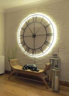 a large clock mounted to the side of a white brick wall next to a wooden bench