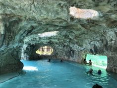 several people are swimming in a large pool with rocks on the sides and water running through it