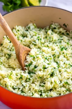 a pot filled with rice and parsley on top of a table next to a wooden spoon