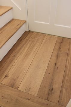 a wooden floor next to a white door and some steps with wood handrails