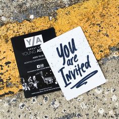 a black and white business card sitting on the ground next to a yellow line with you are invited written on it