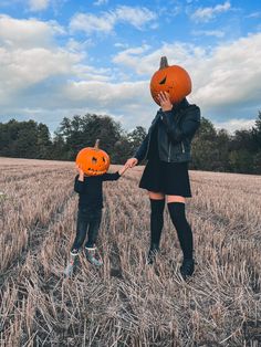 a woman and child holding hands in a field with pumpkins on their heads as they hold hands