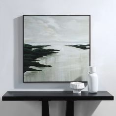 a black and white painting sitting on top of a wooden table next to a vase