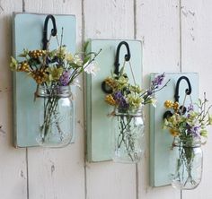 three mason jars with flowers in them are hanging on the wall next to each other