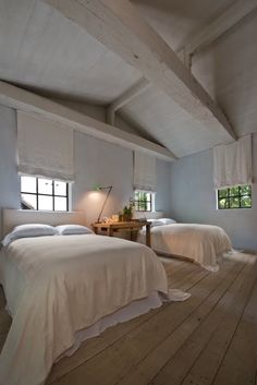 two beds in a room with white linens and wood flooring, one has a lamp on the end table