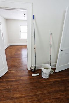 a room with hard wood floors and paint buckets on the floor next to an open door