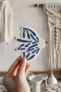 a hand holding up a blue and white fish shaped sticker in front of a wall