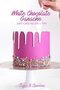 a pink cake with white icing and sprinkles is being cut by a person