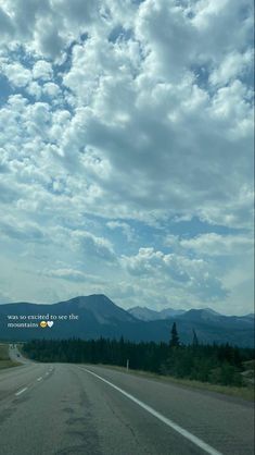 an empty road with mountains in the distance under a cloudy blue sky and white clouds