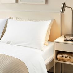 a bed with white sheets and pillows in a bedroom