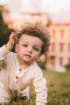 a baby is laying in the grass with his hair flying up and looking at the camera