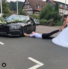 a bride and groom are laying on the ground next to a black car