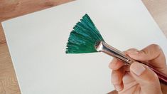 a person is holding a paintbrush and painting a piece of paper with green paint