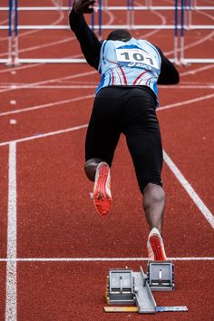 a man jumping over a hurdle on top of a red track with his hands in the air