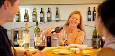 a woman pouring wine into a glass at a table full of cheese and crackers