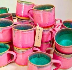 a pile of pink and green coffee mugs sitting next to each other on top of a table