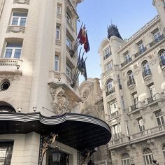 the entrance to an ornate building with flags on it's roof and windows, in front of other buildings