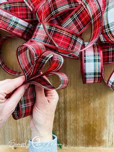 someone is holding up some red and white plaid ribbon on a wooden wall with two hands