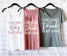 "If you're on the hunt for beach bachelorette party shirts, these Sun Sand and A Ring on My Hand Shirts and matching Sun Sand and A Drink in My Hand shirts are the PERFECT pick for beach bachelorette tank tops! Mix and match the different styles for your wedding party. WHITE TEXT is used by Default or Colored Shirts. ROSE TEXT is used by Default for white Shirts. If you prefer BLACK text for the bride's shirt, please include that in the NOTES section of checkout! HOW TO ORDER 1. Select your quan White Summer Top For Hen Party, Beach Season Tank Top With Letter Print, White T-shirt For Hen Party In Summer, Letter Print Tank Top For Beach Season, White T-shirt For Summer Hen Party, Beach Fitted Tank Top With Letter Print, Fitted Letter Print Tank Top For Beach, Casual Summer Tops For Bachelorette Party, Summer Bachelorette Party T-shirt With Letter Print