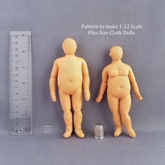 two wooden dolls standing next to each other near a measuring ruler on a gray surface