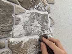 a hand is holding something in front of a wall made out of rocks and cement