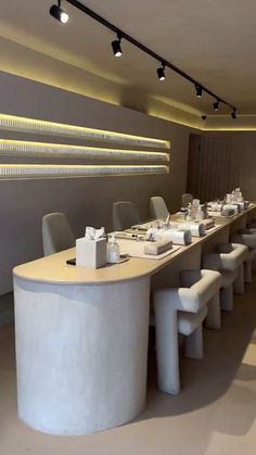 a long table with white chairs is in the middle of an empty room that has lights hanging above it