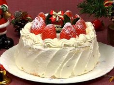 a white cake topped with strawberries on top of a table next to christmas decorations