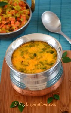 a metal bowl filled with soup next to a wooden cutting board and silver spoons