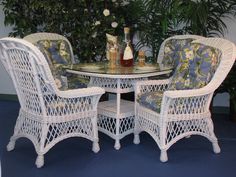 two wicker chairs and a table with bottles on it in front of a potted plant