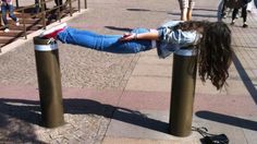 a woman is hanging upside down on poles in the middle of a city street with people walking by