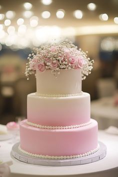 a three tiered cake with pink flowers on top and pearls around the edges, sitting on a table