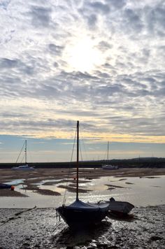 boats are sitting on the muddy shore at low tide, under a partly cloudy sky