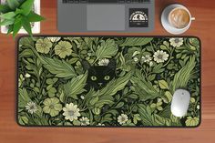 a mouse pad with a black cat surrounded by green leaves and flowers on a wooden desk