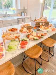 a table filled with lots of food on top of white counter tops next to wooden stools