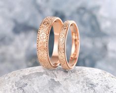 two gold wedding rings sitting on top of a rock next to another ring with filigrees