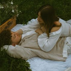 a man and woman laying in the grass with a basket on their back next to each other