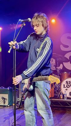 a young man standing on top of a stage holding a guitar and singing into a microphone