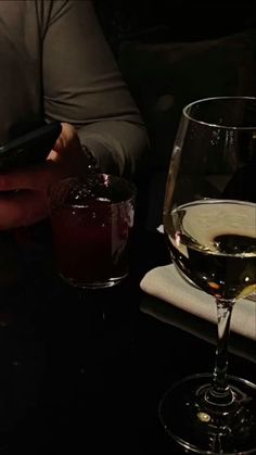 a person sitting at a table with two glasses of wine and a cell phone