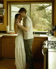 a man and woman standing next to each other in a kitchen near a stove top oven