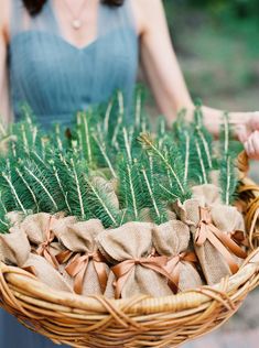 a woman holding a wicker basket filled with pine needles and burlap bows