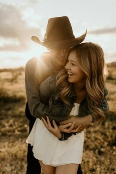 a man in a cowboy hat hugs a woman's chest as the sun shines behind them