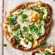 two pizzas with pesto, cheese and an egg on them sitting on a wooden surface