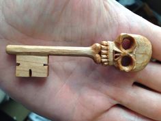 a hand holding a wooden key with a skull on it's end and a bone in the middle