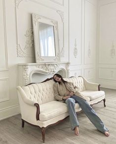 a woman sitting on top of a couch in front of a white fireplace and mirror