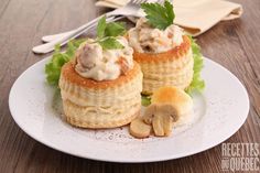 two small pastries on a white plate topped with mushrooms and lettuce leaves